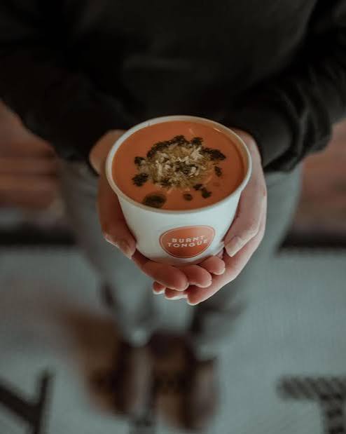 A warm cup of Burnt Tongue soup being handed over